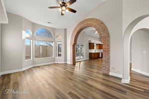 Unfurnished living room featuring arched walkways, dark wood-type flooring, a ceiling fan, and high vaulted ceiling