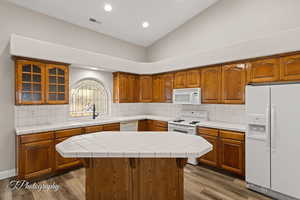 Kitchen with tile counters, white appliances, brown cabinets, backsplash, and vaulted ceiling