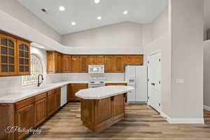 Kitchen with tile countertops, brown cabinetry, decorative backsplash, white appliances, and high vaulted ceiling