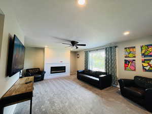 Living area with light carpet, a glass covered fireplace, recessed lighting, and a ceiling fan