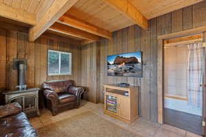 Living area featuring wooden walls, light tile patterned floors, a wood stove, and a wooden ceiling with exposed beams
