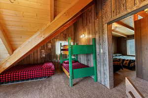 Loft with vaulted ceiling, carpeted floor, and wooden walls and ceiling.