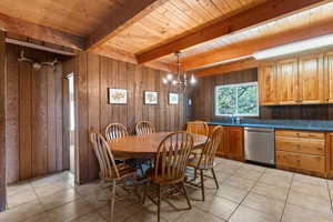 Dining space featuring a chandelier, light tile patterned floors, wooden walls, and a wooden ceiling with exposed beams