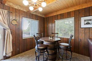 Carpeted dining area featuring wooden walls, a wooden ceiling with exposed beams, and a chandelier