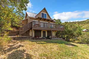 View of property featuring a deck, stairs, a yard, and a metal roof