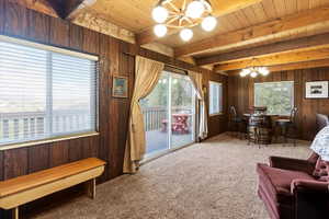 Sitting room with a chandelier, wood walls, carpet floors, and a wood ceiling with exposed beams