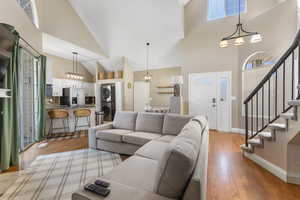 Living area with stairs, high vaulted ceiling, stacked washer / dryer, and light wood-type flooring