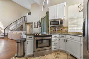 Kitchen with white cabinets, appliances with stainless steel finishes, open floor plan, a peninsula, and decorative backsplash