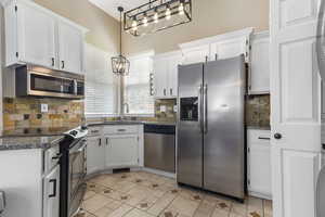 Kitchen featuring appliances with stainless steel finishes, white cabinetry, backsplash, decorative light fixtures, and light tile patterned floors