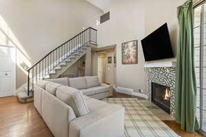 Living area with stairway, light wood finished floors, a tile fireplace, and a towering ceiling