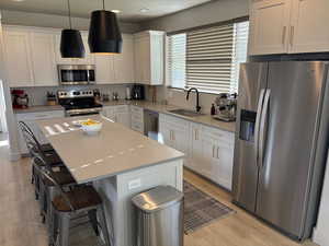 Kitchen with stainless steel appliances, white cabinets, light stone counters, and recessed lighting