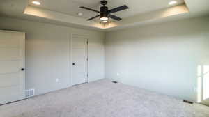 Empty room featuring a raised ceiling, light carpet, recessed lighting, and a ceiling fan
