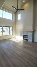 Unfurnished living room with a tiled fireplace, dark wood-type flooring, a towering ceiling, recessed lighting, and ceiling fan