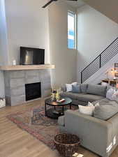Living room featuring a tile fireplace, light wood-type flooring, a high ceiling, and stairs