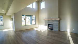Unfurnished living room featuring a tiled fireplace, dark wood finished floors, and a high ceiling
