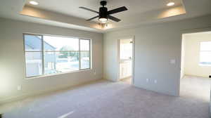 Unfurnished bedroom with a tray ceiling, light colored carpet, a ceiling fan, recessed lighting, and ensuite bathroom
