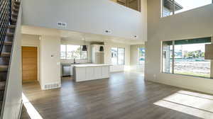 Unfurnished living room featuring dark wood-type flooring, stairway, and a towering ceiling