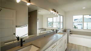 Bathroom with a bath, light wood-type flooring, and double vanity