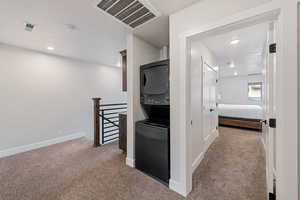 Corridor featuring light carpet, stacked washing machine and dryer, recessed lighting, and an upstairs landing
