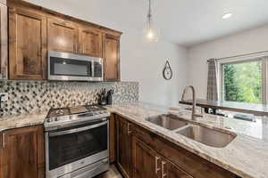 Kitchen with stainless steel appliances, decorative light fixtures, tasteful backsplash, light stone counters, and recessed lighting