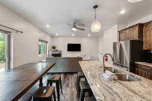 Kitchen with decorative light fixtures, a fireplace, freestanding refrigerator, open floor plan, and light stone countertops