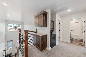 Hallway with recessed lighting, an upstairs landing, light carpet, and stacked washer / dryer
