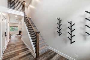 Staircase with a high ceiling, wood finished floors, and a warm lit fireplace