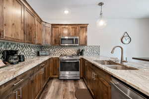 Kitchen with appliances with stainless steel finishes, decorative light fixtures, light stone counters, tasteful backsplash, and dark wood-style flooring