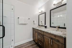 Bathroom with double vanity, a stall shower, and dark wood-style floors