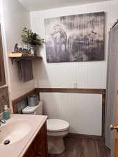 Half bathroom featuring dark wood-style flooring, vanity, and wooden walls