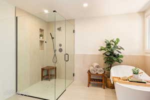 Bathroom featuring a freestanding bath, a shower stall, wainscoting, recessed lighting, and tile walls