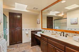 Full bath featuring a shower stall, vanity, tile walls, wainscoting, and a skylight