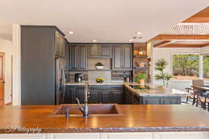 Kitchen with open shelves, tasteful backsplash, butcher block countertops, stainless steel refrigerator with ice dispenser, and beamed ceiling