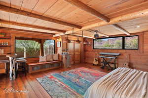 Bedroom featuring wood walls, wood-type flooring, multiple windows, and a wooden ceiling with exposed beams