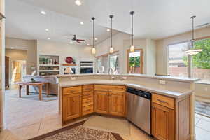 Kitchen with brown cabinetry, a kitchen island with sink, light tile patterned floors, stainless steel dishwasher, and recessed lighting