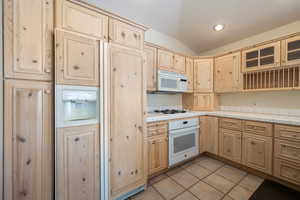 Kitchen with white appliances, light brown cabinetry, tile countertops, a textured ceiling, and light tile patterned floors