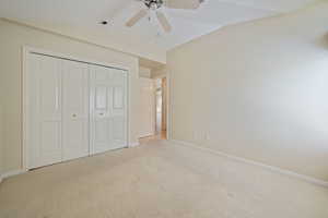 Unfurnished bedroom with vaulted ceiling, carpet, a closet, and ceiling fan
