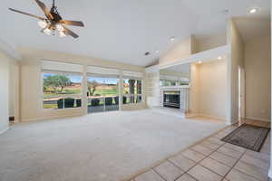 Unfurnished living room with light colored carpet, light tile patterned floors, high vaulted ceiling, a tiled fireplace, and built in shelves