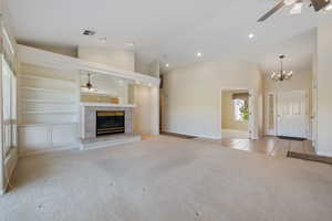 Unfurnished living room with ceiling fan, light colored carpet, built in shelves, light tile patterned floors, and a tiled fireplace