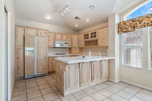Kitchen with light brown cabinets, tile countertops, paneled refrigerator, glass insert cabinets, and light tile patterned flooring