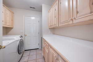 Laundry room with light tile patterned floors, a textured ceiling, separate washer and dryer, and cabinet space