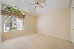 Carpeted spare room featuring vaulted ceiling and ceiling fan