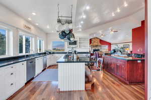 Kitchen featuring a center island with sink, light wood-type flooring, lofted ceiling, a stone fireplace, and open floor plan