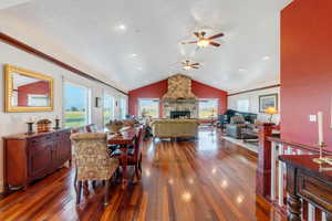 Dining space featuring vaulted ceiling, dark wood-style flooring, a fireplace, and a ceiling fan