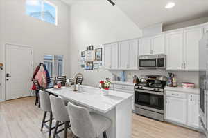 Kitchen featuring stainless steel appliances, white cabinetry, a kitchen bar, light wood-style flooring, and an island with sink