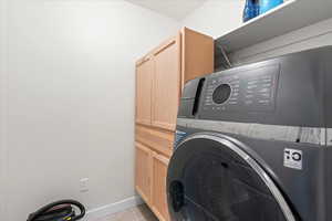 Laundry area with light tile patterned floors and cabinet space