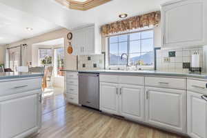 Kitchen with white cabinetry, a mountain view, light wood-style floors, stainless steel dishwasher, and healthy amount of natural light