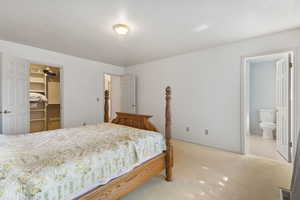 Bedroom with a walk in closet, light colored carpet, a textured ceiling, and connected bathroom