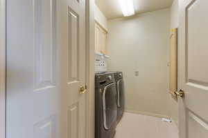 Laundry area featuring light tile patterned flooring, washer and clothes dryer, a textured ceiling, and cabinet space