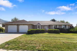 Single story home with a garage, driveway, brick siding, and a front lawn